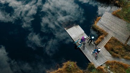 Drei Radfahrer auf einem Steg am See mit Wolkenreflektion im Wasser