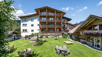Sporthotel Exclusive © Sporthotel Exclusive SAS Großer Garten mit Tischen, Stühlen und Liegestühlen vor Alpenhaus