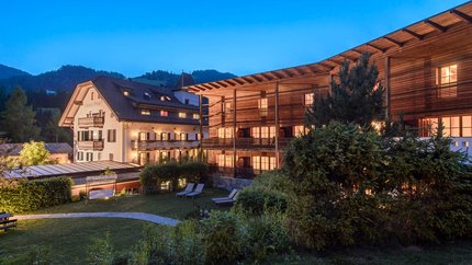 Beleuchtete Hotelgebäude und Garten bei Dämmerung in den Bergen