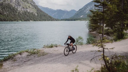 Gravel.Tirol © Liz Kellerer Fahrradfahrer auf Schotterweg neben See und Bergen