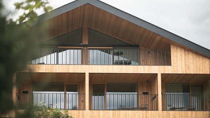 Moderne Holzhausfassade mit Balkonen und Glasfenstern bei bewölktem Himmel