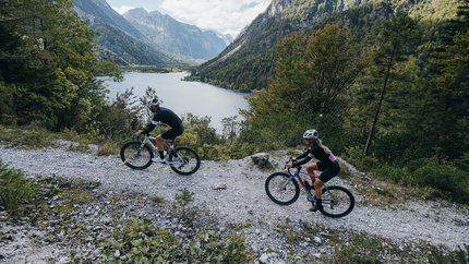 Zwei Radfahrer auf Bergweg mit See und Bergen im Hintergrund