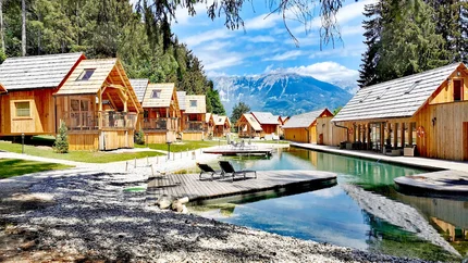 Hotel & Glamping Ribno Alpine Resort © Katarina Strgar Holzhütten am See mit Bergblick und Liegestühlen auf Holzsteg