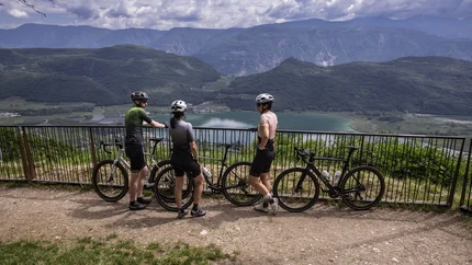 Eppan © Heiko Mandl Drei Radfahrer stehen mit ihren Fahrrädern an einem Geländer und blicken auf einen See und Berge.