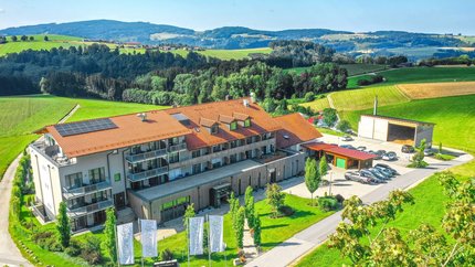 Gebäude mit rotem Dach und Solarzellen umgeben von grüner Landschaft und Hügeln
