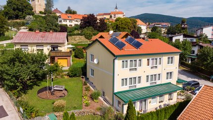 Dorf mit Häusern, Solarpanelen und Burgturm im Hintergrund bei klarem Himmel