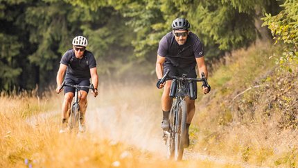 Zwei Männer fahren Mountainbikes auf einem Naturweg im Wald