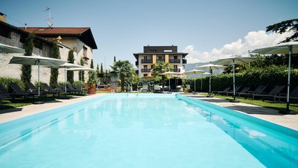 Großer Pool mit Liegestühlen und Sonnenschirmen vor einem modernen Gebäude