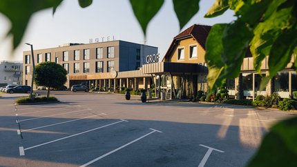 Hotelgebäude mit Parkplatz, teilweise eingerahmt von grünen Blättern bei Sonnenuntergang