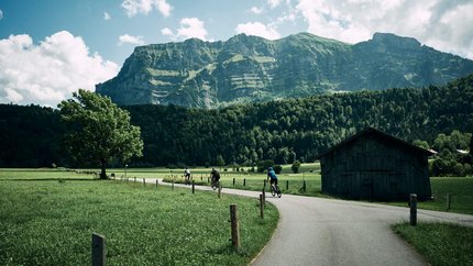 Fahrradfahrer auf Landstraße mit Berg und grünem Feld im Hintergrund