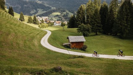 Zwei Radfahrer auf einem Weg im grünen Tal mit Bergen im Hintergrund