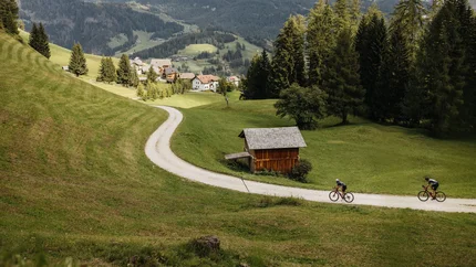 Alta Badia © Alex Moling Zwei Radfahrer auf einem Weg im grünen Tal mit Bergen im Hintergrund