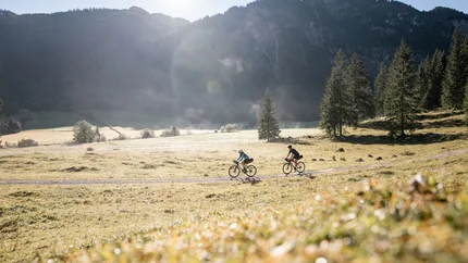 St. Anton am Arlberg © Andreas Vigl Zwei Radfahrer fahren auf einem Feldweg vor Bergkulisse bei Sonnenschein