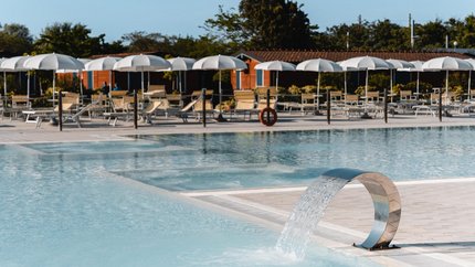 Moderner Pool mit Wasserfontäne und Liegestühlen unter weißen Sonnenschirmen