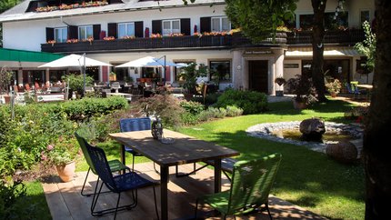 Gartenterrasse mit Tisch, Stühlen und Springbrunnen vor einem Hotel