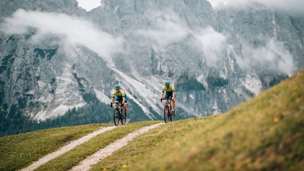 Dolomitenregion Kronplatz © Jens Scheibe Zwei Radfahrer fahren auf einem Bergweg vor nebligen Alpenfelsen