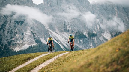 Zwei Radfahrer fahren auf einem Bergweg vor nebligen Alpenfelsen